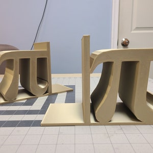 May include: A pair of beige bookends shaped like the mathematical symbol pi.