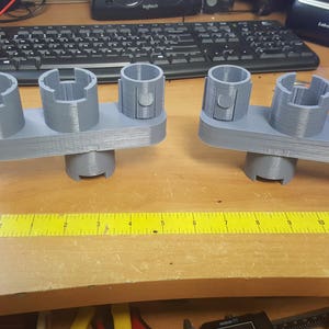 May include: Two gray 3D printed organizers with multiple slots for holding small items. The organizers are made of a smooth, matte plastic and have a slightly textured surface. The organizers are sitting on a wooden table.