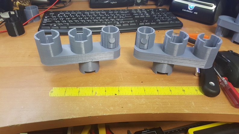 May include: Two gray 3D printed organizers with multiple slots for holding small items. The organizers are made of a smooth, matte plastic and have a slightly textured surface. The organizers are sitting on a wooden table.