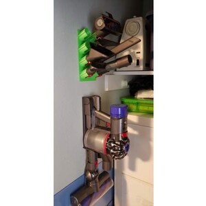 May include: A gray and black cordless vacuum cleaner with a blue and purple attachment is mounted on a wall-mounted holder. The vacuum cleaner is attached to a green wall-mounted storage rack with multiple attachments.