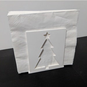 May include: White ceramic napkin holder shaped like a Christmas tree with a star on top. The holder is empty and ready to hold napkins.