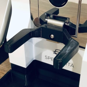 May include: A black 3D printed coffee portafilter holder attached to a white espresso machine with the word "SPECIALITA" printed on the front.