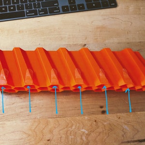 Op de afbeelding: Oranje plastic baan met een honingraatontwerp en acht verhoogde secties. De baan is ontworpen voor speelgoedauto's.
