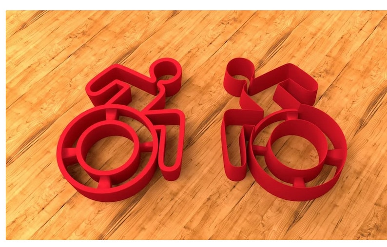May include: Two red plastic cookie cutters shaped like the international symbol for accessibility, depicting a person in a wheelchair.