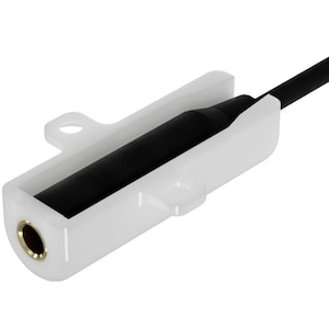 Könnte beinhalten: Ein weißes Kunststoffgehäuse für eine Audiobuchse mit einer schwarzen zylindrischen Komponente und einem schwarzen Kabel, das davon abgeht. Die Buchse hat eine goldfarbene Öffnung. Das Gehäuse hat eine rechteckige Form mit abgerundeten Kanten.