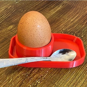 May include: A red plastic egg cup with a brown egg inside and a silver spoon on the side.