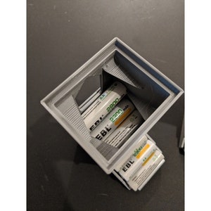 May include: A gray 3D printed battery holder with a stack of AA batteries inside. The batteries are labeled "EBL 2300 mAh".