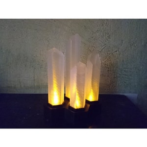 May include: Five white crystal-shaped lamps with warm yellow light glowing from the inside. The lamps are on black bases and arranged in a row.