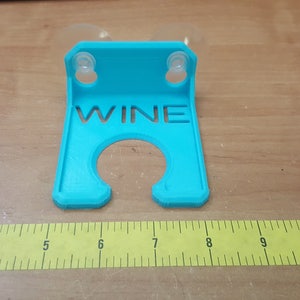 May include: A turquoise blue plastic wine glass holder with suction cups. The holder has the word "WINE" cut out of the front.