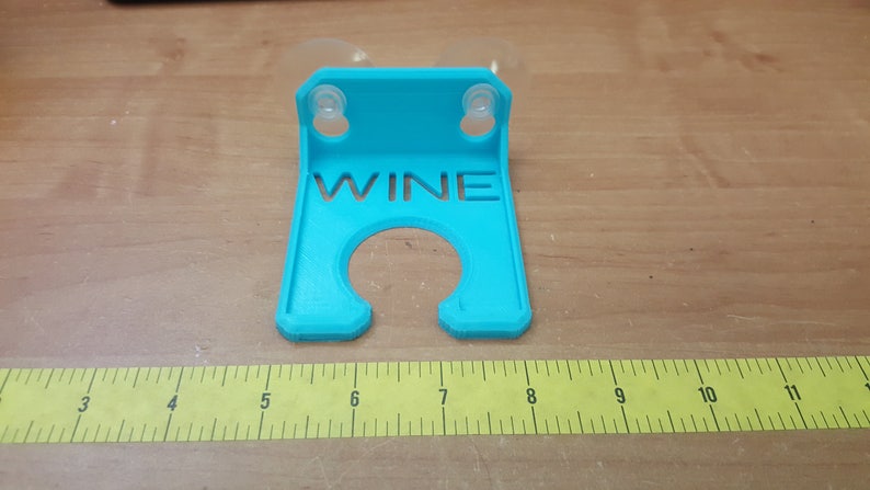 May include: A turquoise blue plastic wine glass holder with suction cups. The holder has the word "WINE" cut out of the front.