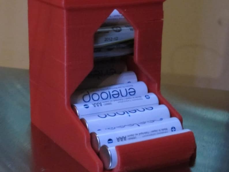 May include: Red plastic battery storage container with a slot for holding AA batteries. The container is filled with Energizer AA batteries.