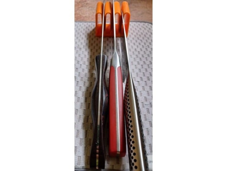 May include: Four knives are stored in an orange plastic knife holder. The knives have black, red, and silver handles.
