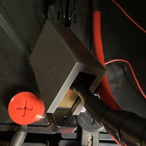 May include: A black plastic box with a red wire coming out of it. The box is connected to a battery terminal. The box is designed to protect the battery terminal from damage.