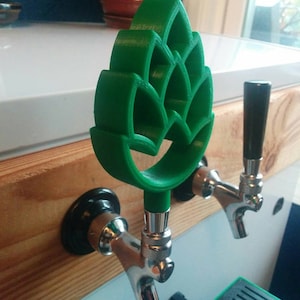 May include: A green 3D printed hop leaf beer tap handle. The handle is attached to a silver tap spout.