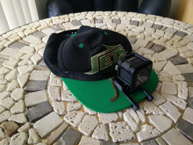 May include: A black and green baseball cap with the word "JETS" in white letters on the front. A black GoPro camera is mounted on the cap.
