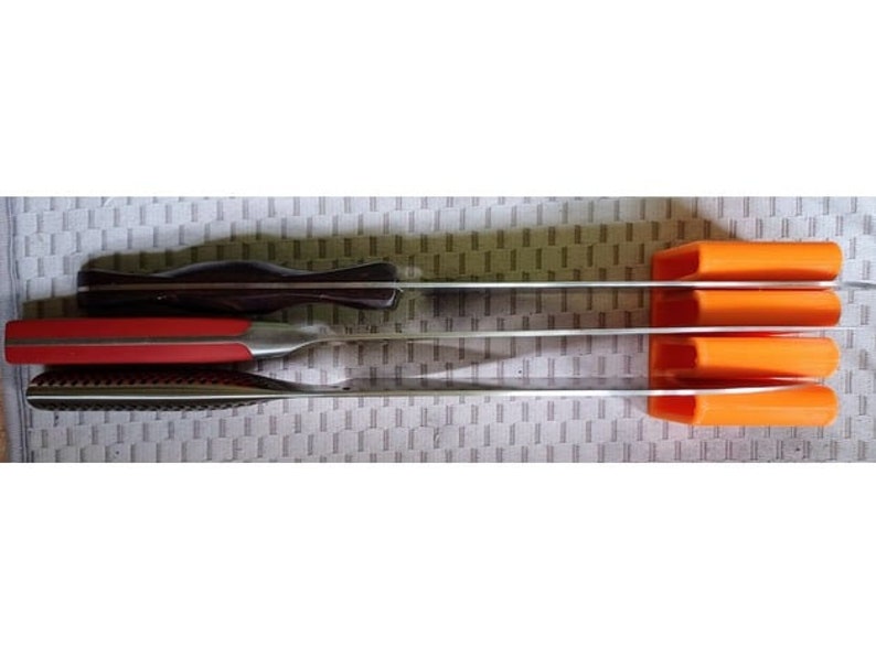 May include: A set of four orange knife holders mounted on a wall, with three knives inserted. The knives are stainless steel with black and red handles.
