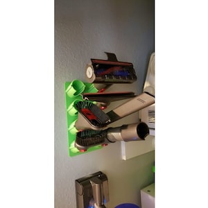 May include: A green wall-mounted organizer with various vacuum cleaner attachments, including a crevice tool, a dusting brush, and a combination tool.