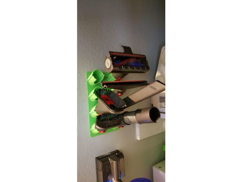 May include: A green wall-mounted organizer with various vacuum cleaner attachments, including a crevice tool, a dusting brush, and a combination tool.