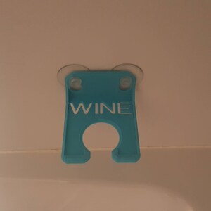 May include: A blue plastic wine glass holder with suction cups. The holder has the word "WINE" printed on it in white.