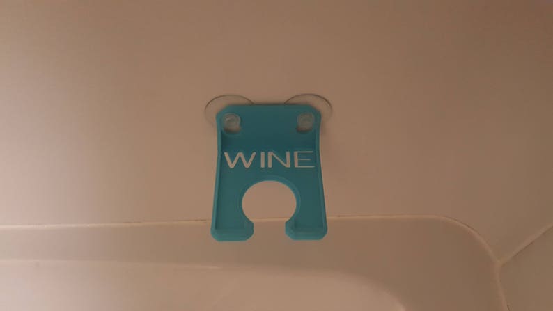 May include: A blue plastic wine glass holder with suction cups. The holder has the word "WINE" printed on it in white.