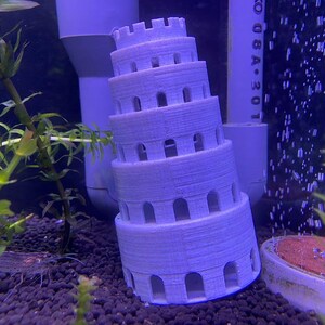 May include: A light purple, multi-tiered tower-shaped aquarium decoration with arched openings. The tower is in an aquarium with green plants and dark gravel. The background includes white pipes and bubbles.