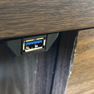 May include: A black USB 3.0 port installed in a wooden surface. The port has a blue interior and gold connectors. The surrounding wood has a dark brown finish.