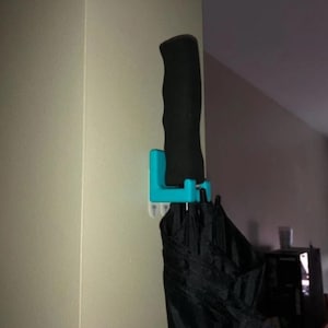 May include: A turquoise plastic umbrella holder mounted on a wall with a black umbrella hanging from it.