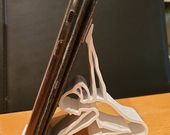 Peut inclure: Support de téléphone en plastique blanc en forme de personne en position de yoga tenant un smartphone noir.