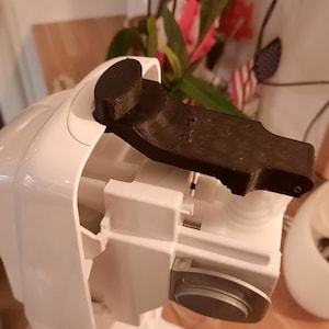 Pode incluir: Um eletrodoméstico branco com uma peça de plástico preto presa na parte superior. A peça preta tem uma forma arredondada e parece ser uma alavanca ou uma alça.