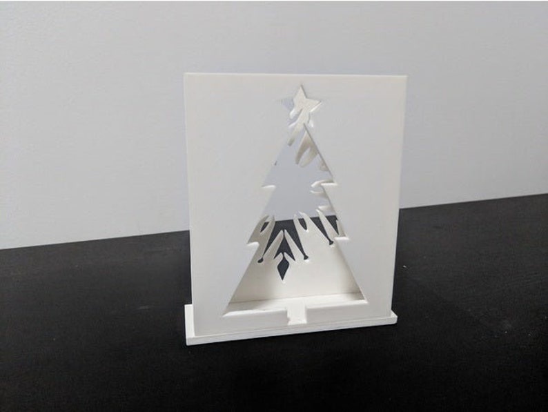 May include: White cardboard cutout of a Christmas tree with a star on top. The tree is designed to be a light holder.