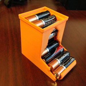 May include: Orange plastic battery storage container with a slot for holding multiple AA batteries. The container is filled with Duracell brand batteries.