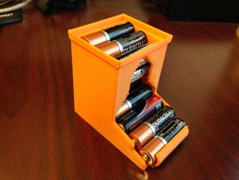 May include: Orange plastic battery storage container with a slot for holding multiple AA batteries. The container is filled with Duracell brand batteries.