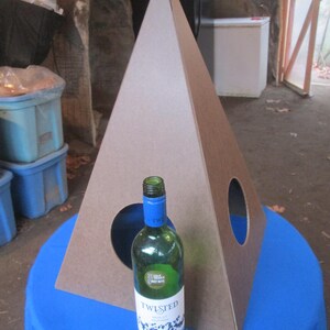 May include: A brown cardboard pyramid with two circular openings. A clear glass bottle of Twisted  wine is in front of the pyramid on a blue tablecloth.