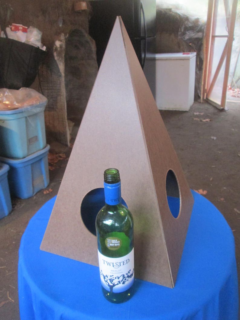 May include: A brown cardboard pyramid with two circular openings. A clear glass bottle of Twisted  wine is in front of the pyramid on a blue tablecloth.