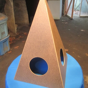 May include: A brown wooden pyramid with two circular openings. The pyramid is sitting on a blue tablecloth.