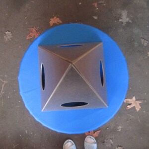 May include: A brown wooden pyramid with four square holes cut out of the sides. The pyramid is sitting on a blue circular surface.
