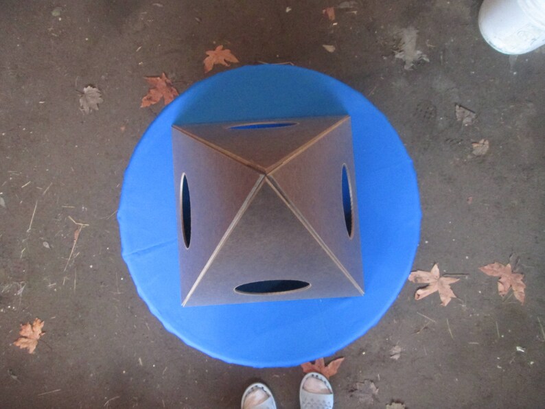 May include: A brown wooden pyramid with four square holes cut out of the sides. The pyramid is sitting on a blue circular surface.