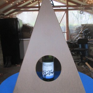May include: A triangular wooden stand with a circular cutout in the center. A bottle of Twisted Merlot wine is placed in the cutout.