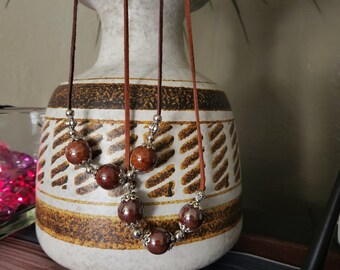 May include: Two brown leather cords with brown and silver beads strung on them. The cords are hanging from a brown and white patterned vase.