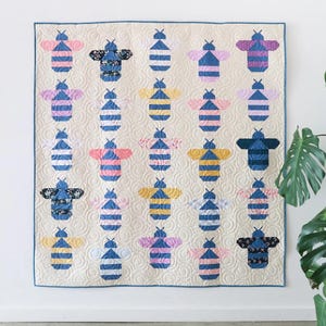 May include: A square quilt featuring a repeating pattern of twenty-five stylized bee shapes arranged in a grid. The bees are constructed from various fabrics in shades of blue, yellow, pink, and floral prints, set against a cream-colored background.
