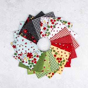 May include: A collection of square fabric swatches arranged in a circular fan pattern. The fabric pieces feature various patterns including red strawberries, green leaves, black and white gingham, polka dots, and floral prints in red, green, and white.