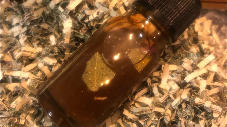 May include: A small, clear glass bottle filled with a dark brown liquid. The bottle is sitting on a bed of shredded paper money.
