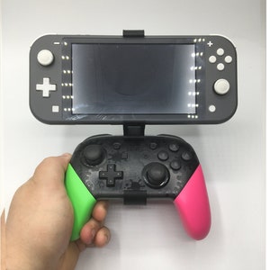 May include: A black Nintendo Switch console with a green and pink controller. The console is attached to a stand and has a black screen.