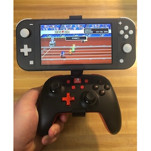 May include: A black and red video game controller with a red plus button and a Nintendo Switch console displaying a video game with the text "TOKYO 1964" on the screen.