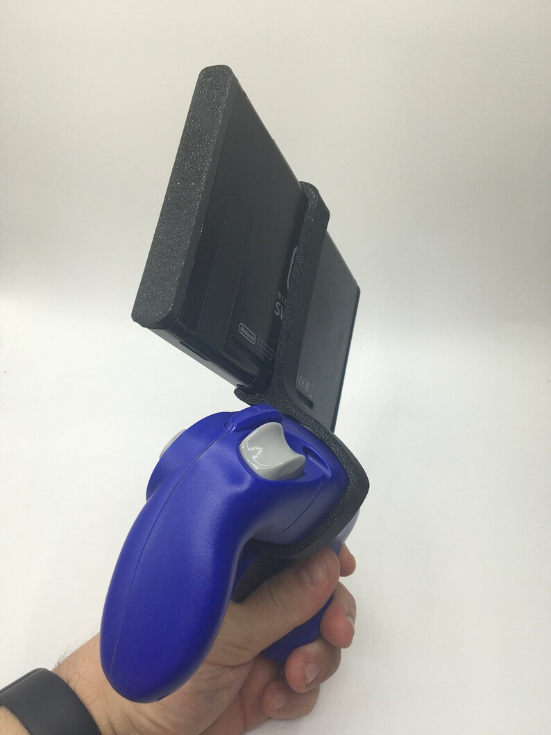 May include: A blue Nintendo GameCube controller attached to a black Nintendo Switch console with a black protective case. The Switch console is held vertically and the controller is held horizontally.