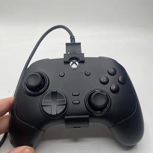 May include: Black Razer Xbox controller with a wired connection. The controller has a D-pad, two analog sticks, and several buttons. The Xbox logo is visible on the top center of the controller.