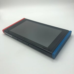 May include: A black Nintendo Switch console with red and blue joy-con controllers. The console is in a closed position.