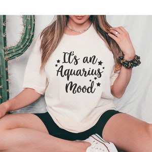 May include: A white t-shirt with the text "It's an Aquarius Mood" in black lettering with stars around the text.