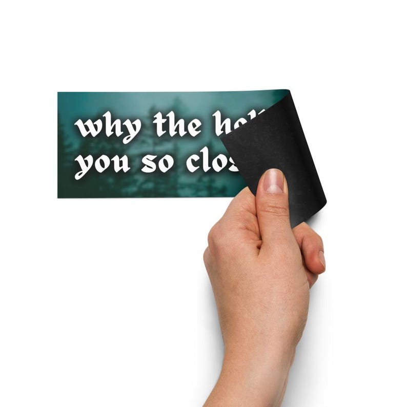 May include: A rectangular sticker with the text "why the hell you so close" in white, stylized font. The background is a blurred teal and green forest scene. A hand is peeling back a corner of the sticker, revealing a black adhesive backing.