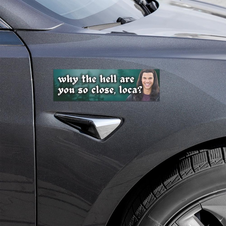 May include: A rectangular bumper sticker with the text "why the hell are you so close, loca?" in white font. The sticker features a photo of a smiling person. The sticker is attached to a gray car.